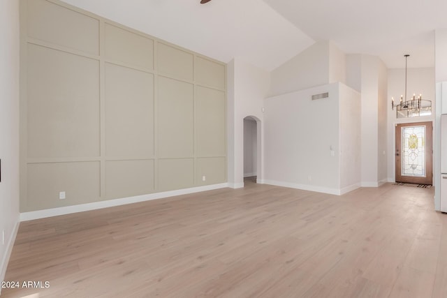 unfurnished living room featuring an inviting chandelier, high vaulted ceiling, and light hardwood / wood-style flooring