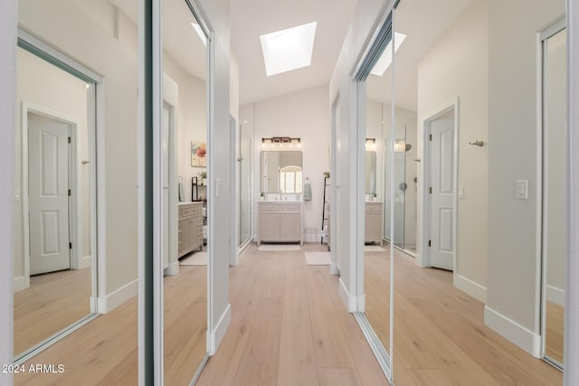 hall with lofted ceiling with skylight and light hardwood / wood-style floors