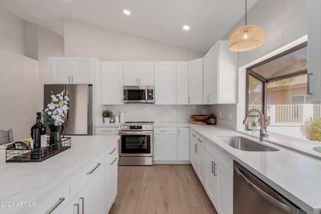 kitchen featuring white cabinets, sink, hanging light fixtures, vaulted ceiling, and stainless steel appliances