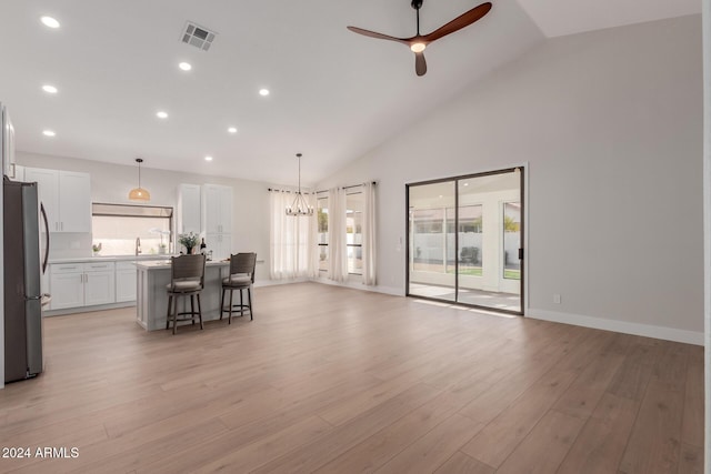 unfurnished living room featuring ceiling fan with notable chandelier, light wood-type flooring, sink, and high vaulted ceiling