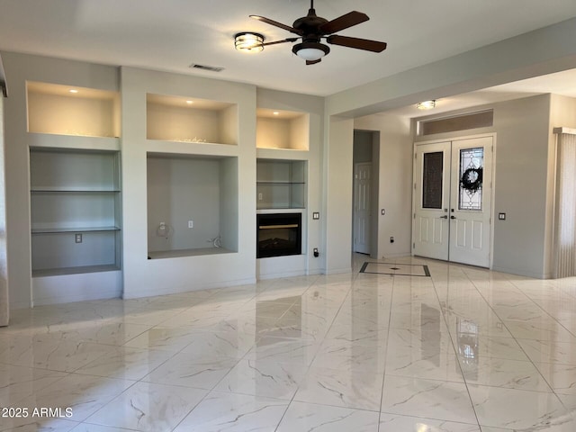 unfurnished living room with ceiling fan and built in shelves