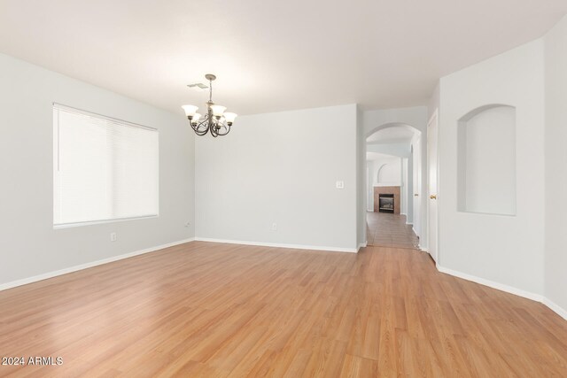 spare room featuring a chandelier, a tiled fireplace, and light hardwood / wood-style flooring