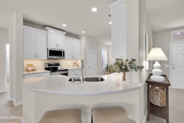 kitchen with a kitchen bar, sink, white cabinetry, appliances with stainless steel finishes, and decorative backsplash