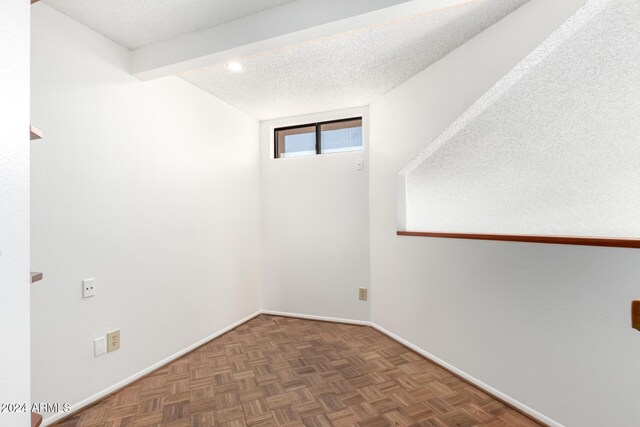 unfurnished room featuring dark parquet floors, beamed ceiling, and a textured ceiling