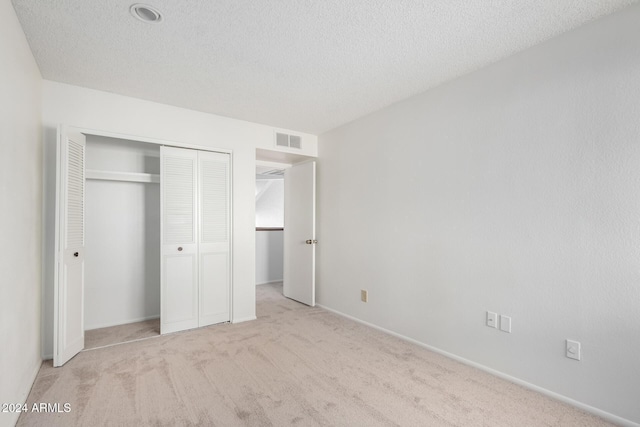 unfurnished bedroom featuring light carpet, a closet, and a textured ceiling