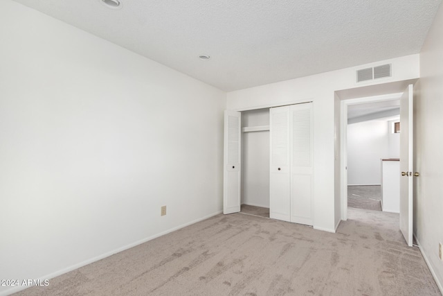 unfurnished bedroom with a textured ceiling, light colored carpet, and a closet