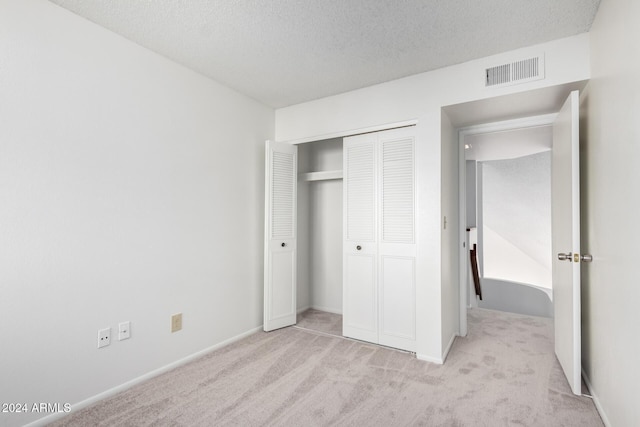 unfurnished bedroom with light carpet, a textured ceiling, and a closet