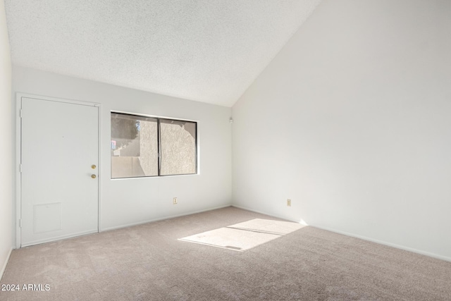 spare room featuring a textured ceiling, light carpet, and lofted ceiling