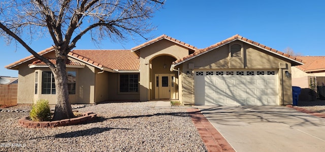 mediterranean / spanish house featuring stucco siding, driveway, a tile roof, fence, and a garage