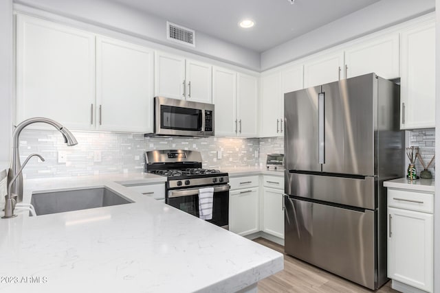 kitchen with sink, white cabinetry, stainless steel appliances, light stone countertops, and decorative backsplash