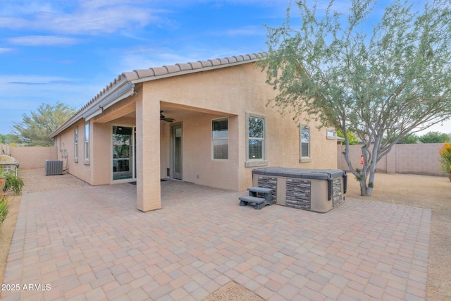 rear view of property with a ceiling fan, a fenced backyard, a hot tub, and stucco siding