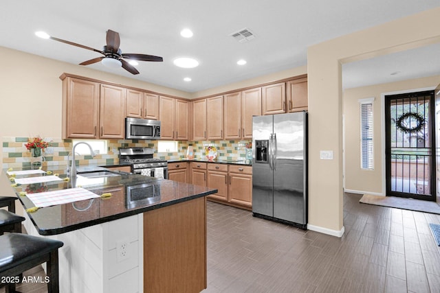 kitchen featuring a peninsula, appliances with stainless steel finishes, light brown cabinetry, and tasteful backsplash