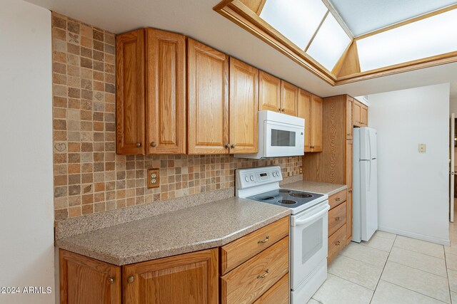 kitchen featuring decorative backsplash, light tile patterned floors, a skylight, and white appliances