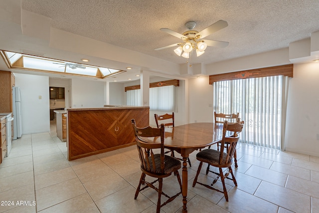 tiled dining space featuring a raised ceiling, a textured ceiling, a skylight, and ceiling fan