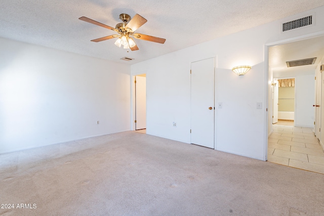 unfurnished bedroom featuring light carpet, a textured ceiling, and ceiling fan