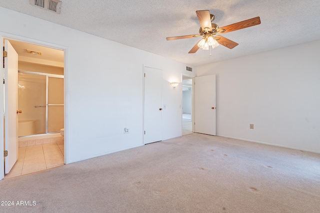 unfurnished bedroom featuring a textured ceiling, ensuite bathroom, light colored carpet, and ceiling fan