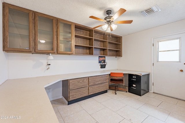 tiled office space featuring built in desk, a textured ceiling, and ceiling fan