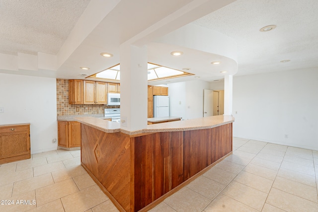 kitchen featuring white appliances, a skylight, backsplash, kitchen peninsula, and light tile patterned floors