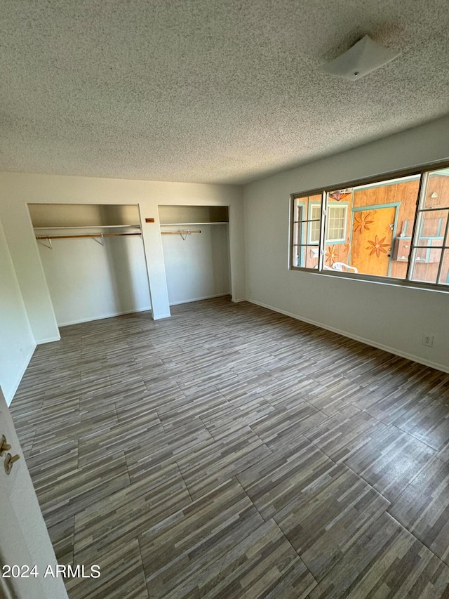 unfurnished bedroom featuring multiple closets, dark wood-type flooring, and a textured ceiling