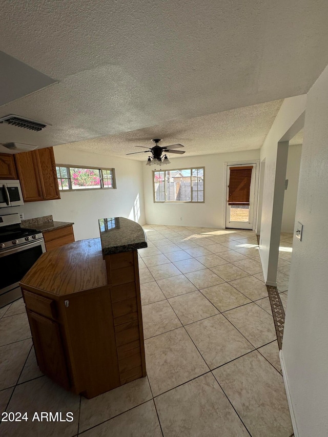 kitchen with appliances with stainless steel finishes, light tile patterned flooring, a textured ceiling, a center island, and ceiling fan