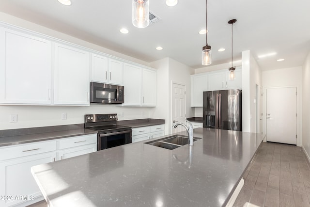 kitchen with appliances with stainless steel finishes, a kitchen island with sink, light wood-type flooring, sink, and decorative light fixtures