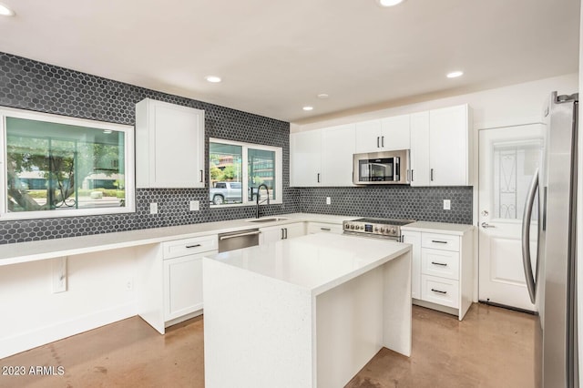 kitchen with sink, appliances with stainless steel finishes, white cabinetry, backsplash, and a kitchen island