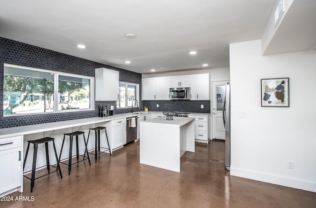 kitchen with a kitchen bar, sink, white cabinetry, a center island, and appliances with stainless steel finishes