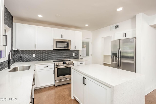 kitchen featuring sink, appliances with stainless steel finishes, white cabinetry, backsplash, and a center island