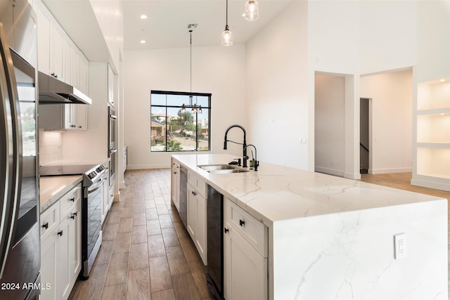 kitchen featuring a kitchen island with sink, sink, light stone countertops, decorative light fixtures, and stainless steel appliances