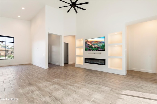 unfurnished living room featuring ceiling fan and a high ceiling