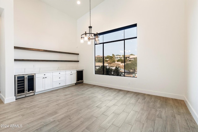 unfurnished living room featuring lofted ceiling, wine cooler, and a chandelier