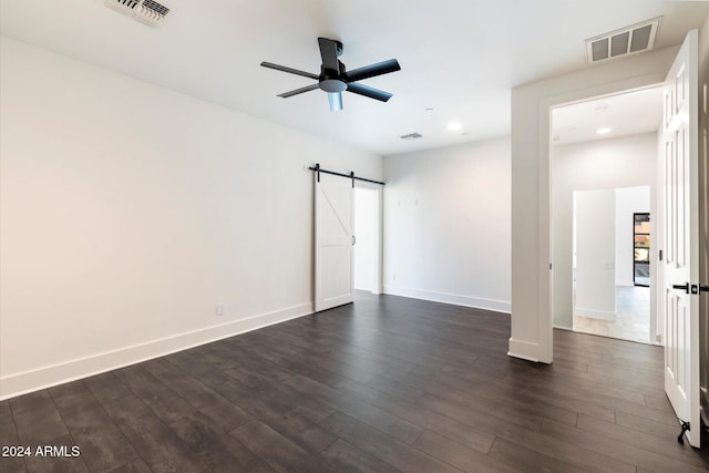 unfurnished bedroom with a barn door, dark hardwood / wood-style floors, and ceiling fan