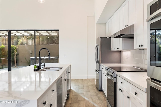 kitchen with backsplash, sink, light stone counters, white cabinetry, and stainless steel appliances