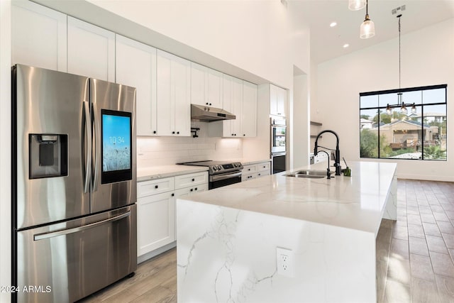 kitchen featuring appliances with stainless steel finishes, light stone counters, a kitchen island with sink, sink, and hanging light fixtures