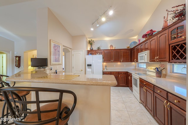 kitchen with a breakfast bar area, vaulted ceiling, light tile patterned floors, kitchen peninsula, and white appliances