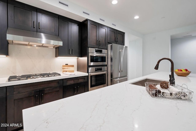 kitchen with appliances with stainless steel finishes, decorative backsplash, dark brown cabinetry, and light stone countertops