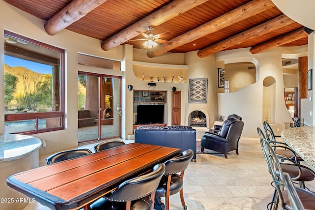 dining room featuring a warm lit fireplace, visible vents, wooden ceiling, beamed ceiling, and a mountain view