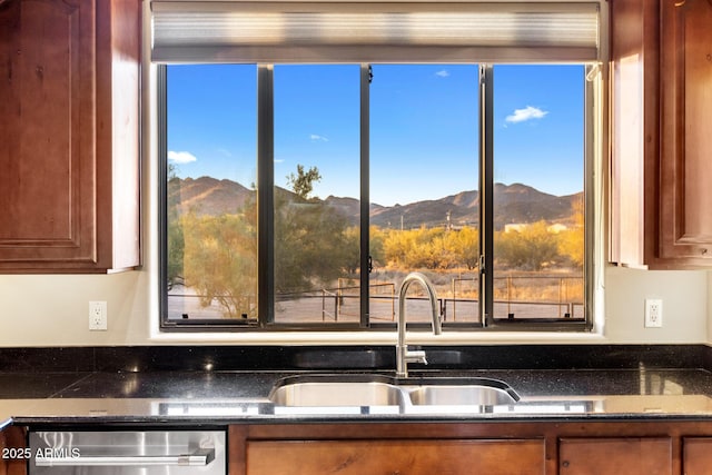 kitchen with brown cabinets, dark stone countertops, a sink, a mountain view, and stainless steel dishwasher