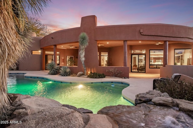 pool at dusk featuring ceiling fan, an outdoor pool, and a patio