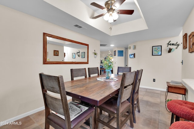 tiled dining area with ceiling fan and a raised ceiling