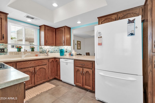 kitchen with sink, white appliances, a tray ceiling, decorative backsplash, and light tile patterned flooring