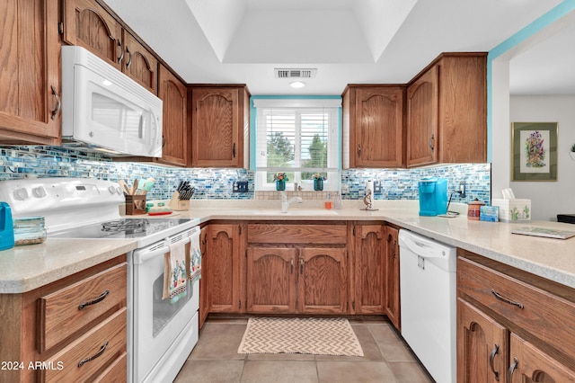 kitchen featuring a raised ceiling, backsplash, light tile patterned floors, and white appliances