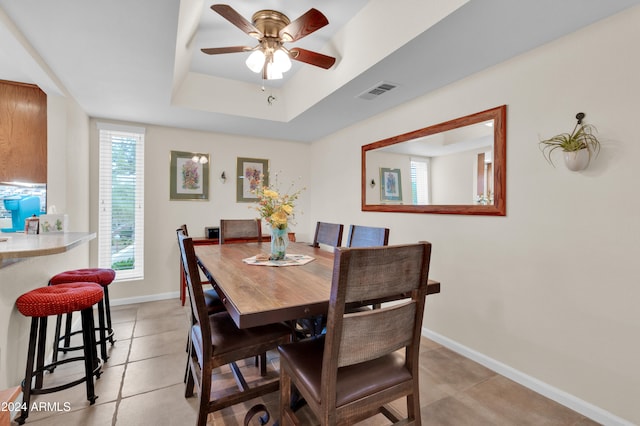 tiled dining space with a tray ceiling and ceiling fan