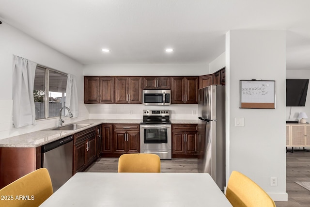 kitchen featuring recessed lighting, stainless steel appliances, a sink, light wood-style floors, and dark brown cabinets