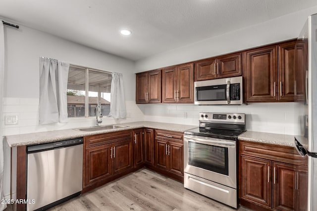 kitchen featuring light wood finished floors, tasteful backsplash, light countertops, appliances with stainless steel finishes, and a sink