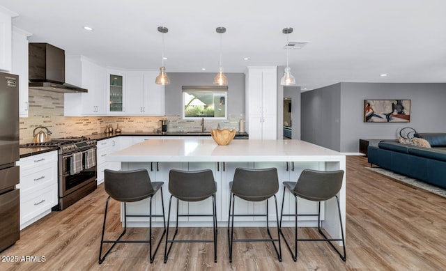 kitchen featuring pendant lighting, white cabinets, stainless steel range with gas cooktop, and wall chimney range hood