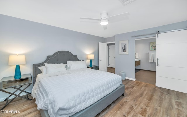 bedroom with hardwood / wood-style flooring, a barn door, ceiling fan, and ensuite bathroom