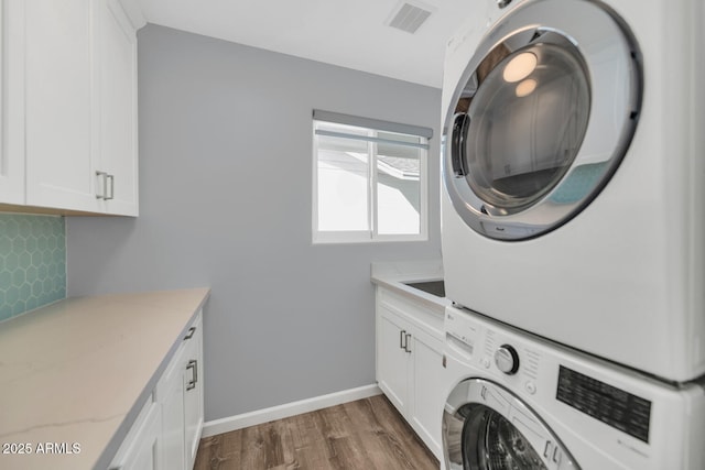 washroom featuring cabinets, stacked washer and dryer, and dark hardwood / wood-style floors