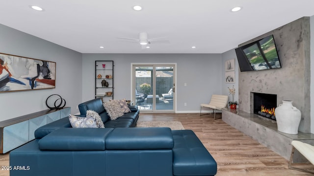 living room featuring ceiling fan, a fireplace, and light wood-type flooring