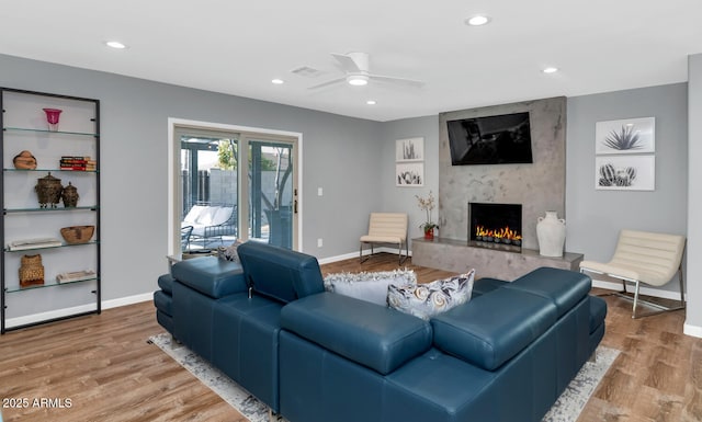 living room with ceiling fan, a high end fireplace, and light hardwood / wood-style flooring